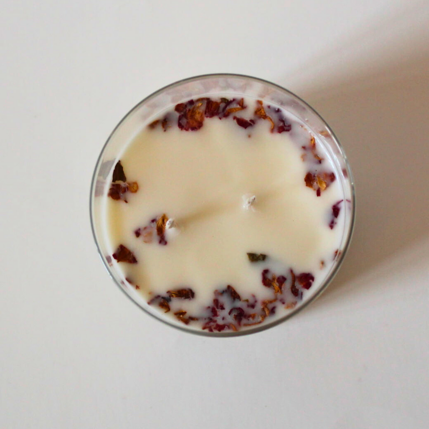 Candle with dried rose petals in a glass container on a white background